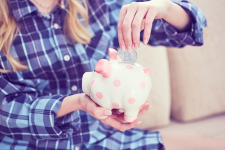 Young girl sitting on couch and putting litecoin in piggybank.の写真素材