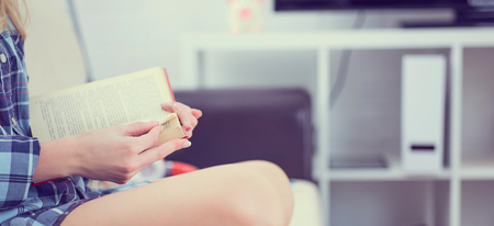 Close - up of a book in the hands of a girl sitting on the couch on home interior backgroundの写真素材