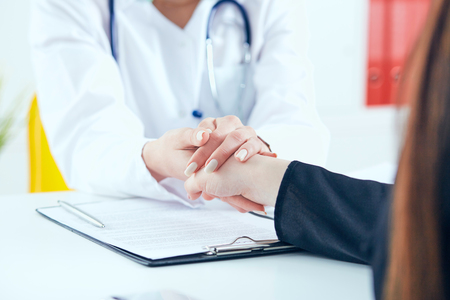 Friendly female doctors hands holding female patients hand for encouragement and empathy close-up. Partnership, trust and medical ethics concept.の写真素材