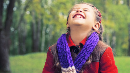 Autumn portrait of the nice smiling little girl in red coat. In her hands a bouquet of yellow maple...