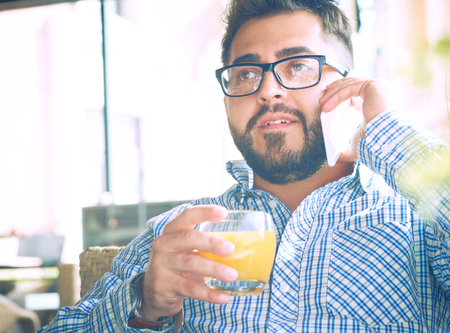 Handsome man with glasses drinking juice and looking at mobile phone in cafe.の写真素材