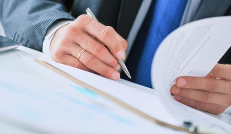 Businessman in dark suit sitting at office desk signing a contract with shallow focus on signature.