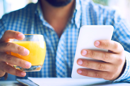 Handsome man with glasses and beard drinking juice and looking at mobile phone in cafe.の写真素材