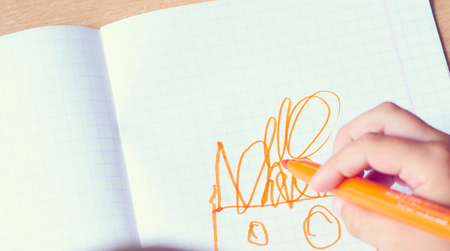 Childs hand draws in a notebook with orange felt-tip pen. Childrens creativity.の写真素材