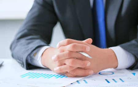 Businessman at the table at a business meeting with his hands clasped and holding a pen, listening carefully to the report of colleagues.の写真素材