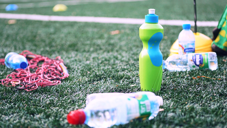 Plastic bottles with blurry soccer training equipment on artificial turf. It is waste from soccer...