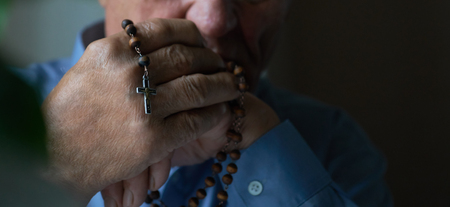 Praying hands of an old man holding rosary beads.の写真素材