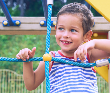 Little Caucasian boy in striped t-shirt hang the blue bar by his hand to exercise at out door playground in summer day.の写真素材