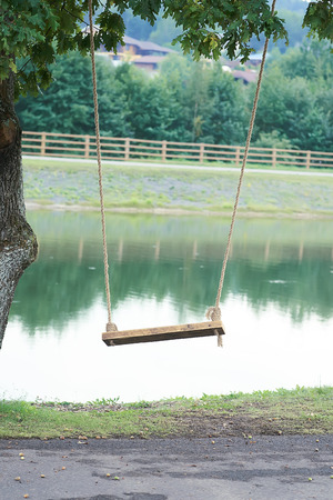 Wooden swing on a rope mount mounted on a tree on the shore of the lake.の写真素材