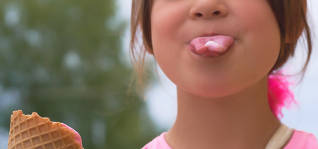 Little girl with waffle cone ice cream shows her rose tongue.