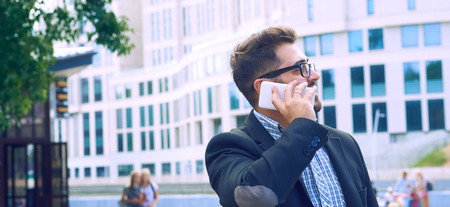 Young businessman in glasses with a beard talking on the phone walking down the street.の写真素材