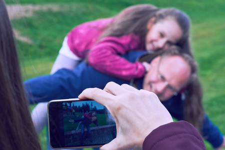 Female hands using mobile phone for taking family photo of her husband and daughter.の写真素材
