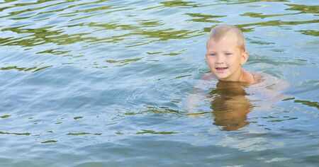 Little Caucasian boy in swimming goggles swimming in the lakeの写真素材