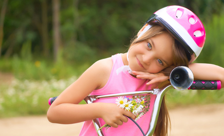 Portrait of a little girl in a protective helmet controls her bike and holds a bouquet of daisies.の写真素材