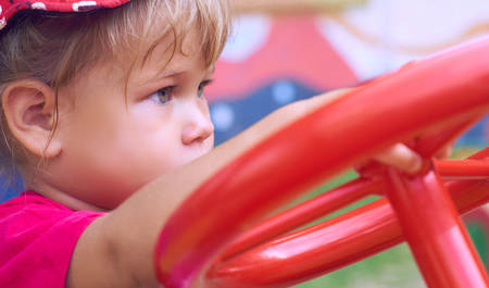 Little Caucasian baby girl sits at the wheel of a toy car. Playing on the playground concept.の写真素材