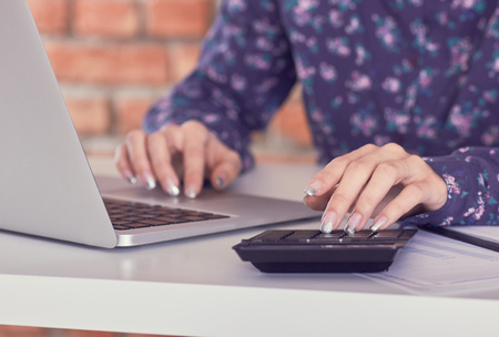 Woman working with calculator, business documents and laptop computer close-up.
