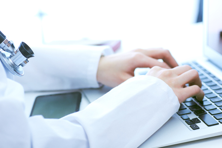 Close-up of female doctor hands typing on laptop computer while sitting at the desk in hospital office.の写真素材