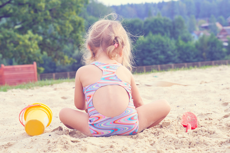Little blonde baby girl playing with sand on the beach using plastic toys.の写真素材