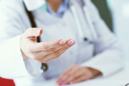 Female doctor making welcome gesture, politely inviting patient to sit down in medical office close-up.の写真素材
