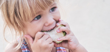 Cute adorable toddler girl eating fresh pear sitting on the beach.の写真素材
