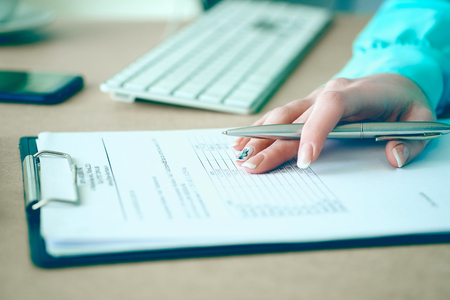 Hand of businesswoman filling and signing with silver pen partnership agreement form clipped to pad close-up. Management training course, some important document, team leader ambition conceptの写真素材