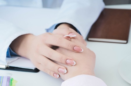 Friendly female doctor hands holding patient hand sitting at the desk for encouragement, empathy, cheering and support while medical examination. Just hands over the table.の写真素材