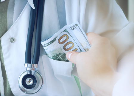 Medicine doctor receiving amount of dollar banknotes as a bribe. Corruption in health Care industry concept.の写真素材