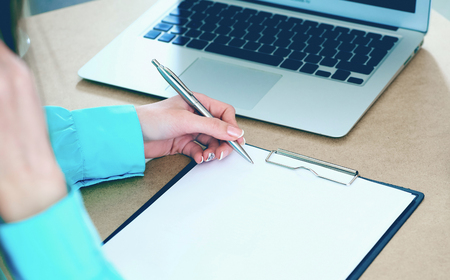 Stressed business woman write in clipboard in the surrounding of laptop and crumpling paper at her table in the office. Woman trying to come up with the right solutionの写真素材