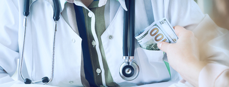 Medicine doctor receiving amount of dollar banknotes as a bribe. Corruption in health Care industry concept.の写真素材