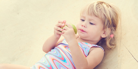 Cute adorable toddler girl eating fresh pear lying on the beach.の写真素材