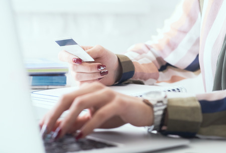 Female office worker hands holding credit card, typing on the keyboard of laptop, online shopping detail close up.の写真素材