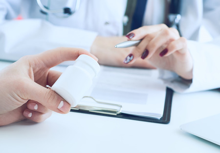 Female medicine doctor hand hold silver pen and points to a jar of pills in patients hand.Young doctor talks to patient about the properties of the drug.の写真素材