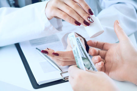 Female doctor hands gives jar of pills to patient hand and receives money in return closeup.の写真素材