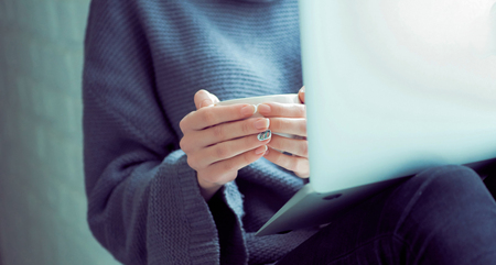 Girl sending a message, e-mail, woman typing something on the laptop in her lap sitting near window...
