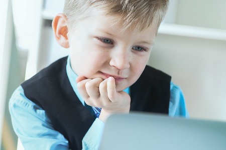 Small cute boy in business suit works at computer at office and smiling. Small business man, little boss.の写真素材