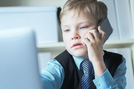 Young confident executive businessman boss boy in office talks on the phone sitting at the desk with laptop.の写真素材