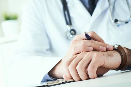 Man doctor with stethoscope looking at wrist watch. Doctor in white uniform at office background waiting for patients. Time to visit therapist.の写真素材
