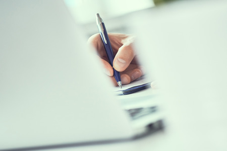 Businessman hand writing note on a notebook. Business man working at office desk. Close up of empty notebook on a blackboard with office supplies.の写真素材