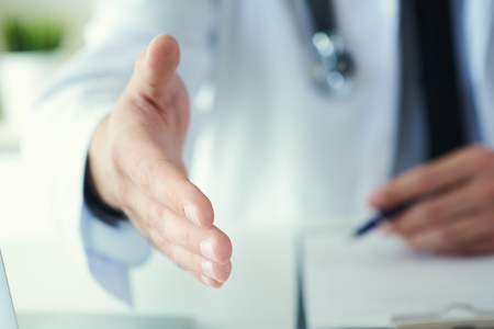 Male medicine doctor offering hand to shake in office closeup. Greeting and welcoming gesture. Medical cure and tests advertisement concept.の写真素材