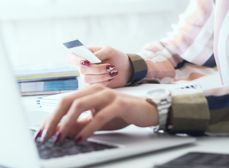 Female office worker hands holding credit card, typing on the keyboard of laptop, online shopping detail close up.の写真素材