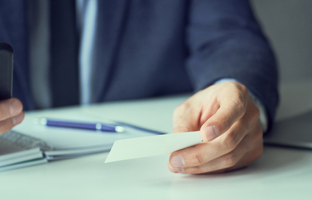 Businessman holding blank business card and dialing numbers on mobile phoneの写真素材