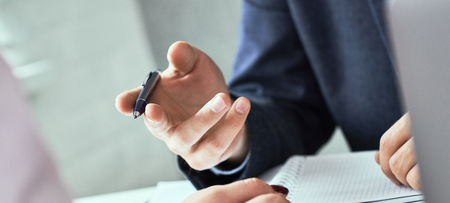 Close up focus on male hand holding ballpoint and explaining something colleague or employee. Corporate team training, negotiations, business seminar job interview conceptの写真素材