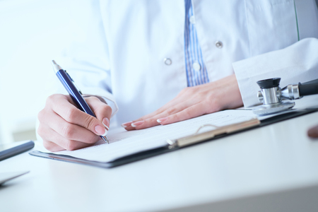 Female medicine doctor hand holding silver pen writing something on clipboard closeup.の写真素材