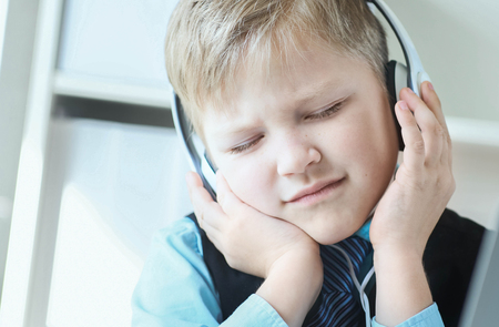 Cute 6 year old boy in suit listening to music or audio tutorial on headphones at the office background.の写真素材