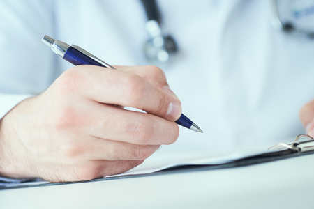 Male physician medicine doctor or pharmacist writing prescription on special form sitting at worktable. Medical care, pharmacy or health insurance concept.の写真素材