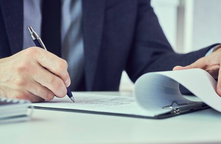 Hand of businessman in suit filling and signing with blue pen partnership agreement form clipped to pad closeup. Management training course, some important document, team leader ambition concept.の写真素材