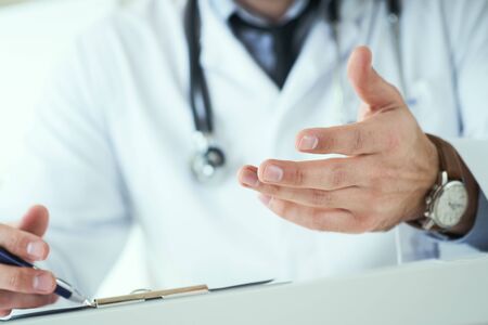 Male doctor making welcome gesture, politely inviting patient to sit down in medical office. Photo with depth of field.の写真素材