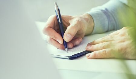 Businessman hand writing note on a notebook close-up. Business man working at office desk. Close up of empty notebook on a blackboard with office supplies.の写真素材