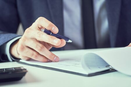 Corporate man with pen in hand working in modern office, signing business document on desk. close up.Businessman reading rental contract before making a deal.の写真素材