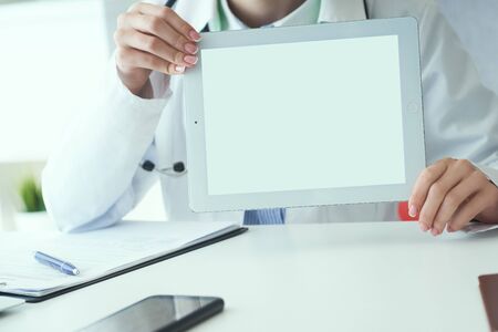 Middle section of female medicine doctor shows tablet computer with white screen. Contact...